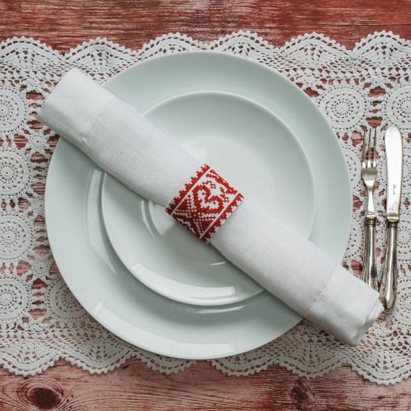 red and white cross stitch napkin ring with a white napkin on white china on lace table cloth with silver cutlery